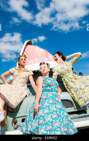 Tres jóvenes mujeres vestidas de retro 50's ama de casa estilo americano vestidos de verano levitas feliz posando para las fotos de las vacaciones con un clásico autocaravana UK Foto de stock