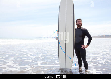 Retrato de joven surfista de pie en el mar con tablas de surf