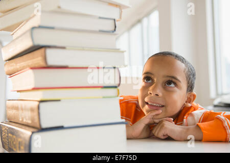 Mestizos niño mirando hacia arriba en la pila de libros