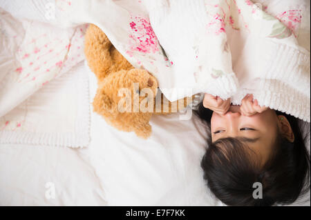 Chica filipina jugando con osito de peluche en la cama