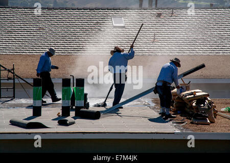 El vapor se eleva desde el alquitrán caliente como obreros hispanos sustituir un garaje techo en Laguna Niguel, CA. Nota rollos de papel de alquitrán. Foto de stock