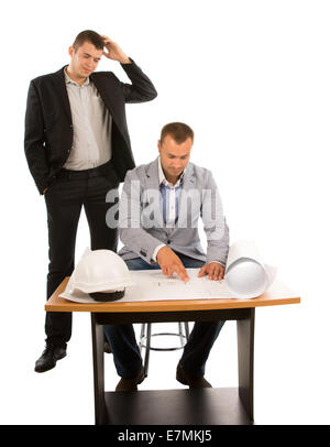 Dos arquitectos o constructores trabajan en un plan como un equipo para tratar de resolver un problema con uno sentado en una mesa y el otro pie rascándose la cabeza, aislado en blanco.