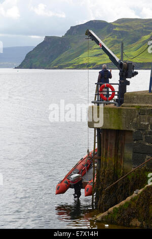 Un hombre bajando una pequeña embarcación inflable en Portree Harbour en la Isla de Skye, Scottish Highlands, Escocia. Foto de stock