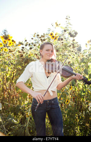 Mujer joven tocando el violín en campo de girasol