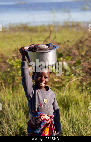 Un niño lleva un balde de pescado en una aldea de pescadores de Bangweulu Wetlands, Zambia Foto de stock