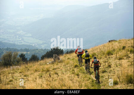 Tres ciclistas de montaña en el camino cuesta abajo, Matajur, Istria, Eslovenia Foto de stock