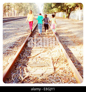 Cuatro niños caminando por vías de ferrocarril abandonadas con las manos, California, Estados Unidos
