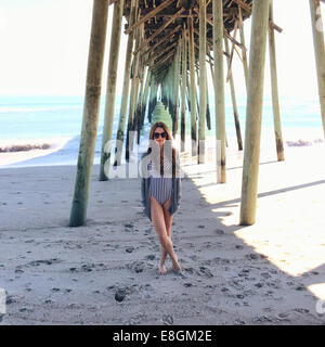 Mujer de pie en la playa bajo un muelle de madera, Carolina Beach, Carolina del Norte, Estados Unidos