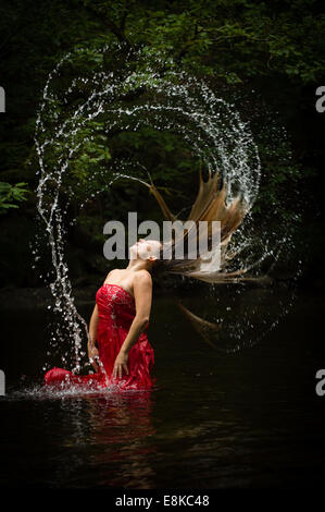 La sucesión de Fibonacci: Una mujer de pelo rubio vestida de un rojo profundo levita vestido en un río moviéndo voltear su cabello Foto de stock