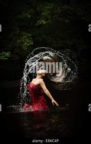 La sucesión de Fibonacci: Una mujer de pelo rubio vestida de un rojo profundo levita vestido en un río moviéndo voltear su cabello Foto de stock