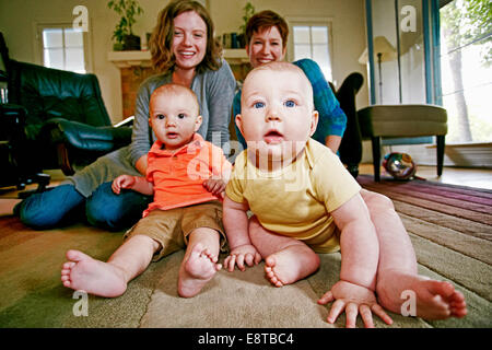 Las madres y los bebés caucásicos sentados en el suelo del cuarto de estar