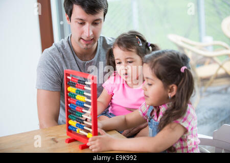 Padre e hijas jugando con abacus en casa Foto de stock
