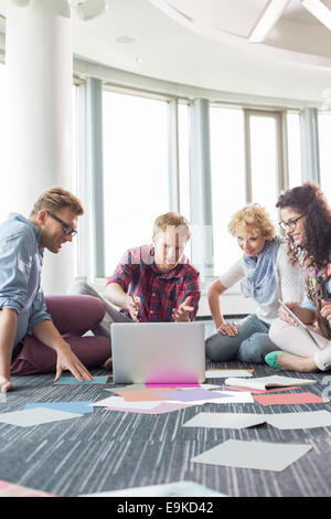 Los empresarios utilizando el portátil mientras está sentado en el piso en la oficina creativa