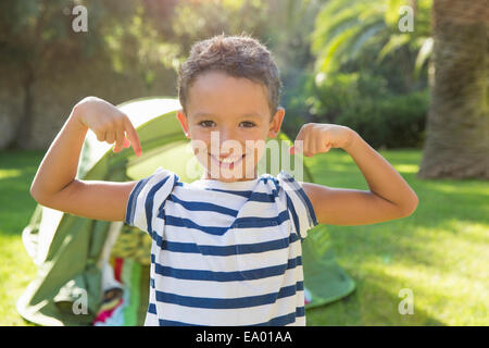 Retrato de niño en jardín flexionando los músculos