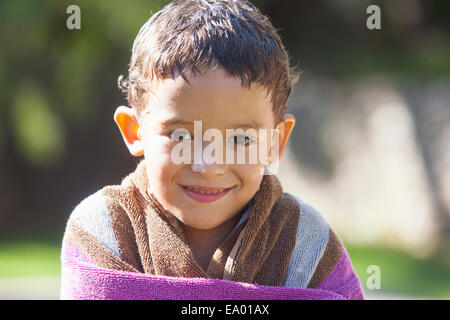 Retrato de niño con cabello envuelto en una toalla mojada en el jardín