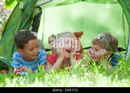 Tres niños acostado charlando en el jardín de su tienda Foto de stock