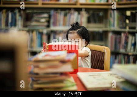 Niña de un año, libro de lectura en la biblioteca Foto de stock