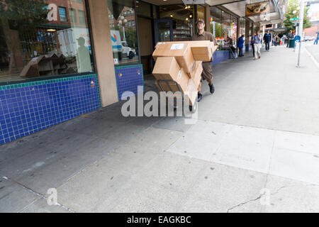 Controlador de entrega de UPS empujando una carreta de mano / camión lleno de paquetes de cartón en una acera Foto de stock