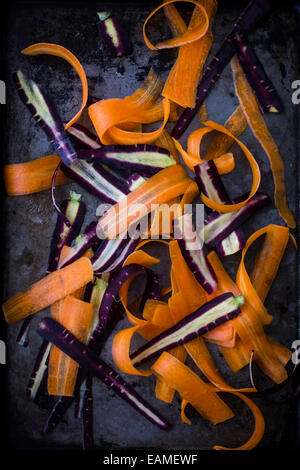 Morado y naranja zanahorias, afeitado, en bandeja oscura