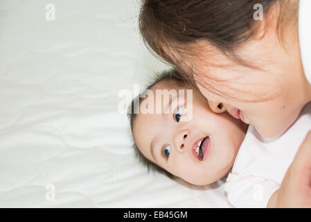 Feliz alegre familia. La madre y el bebé asiático besarse, riendo y abrazando a Foto de stock