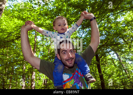 Padre feliz que lleva al hijo en los hombros debajo de los árboles escena verde Foto de stock