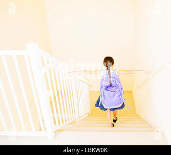 Chica (6-7) con mochila caminando por las escaleras en su casa Foto de stock