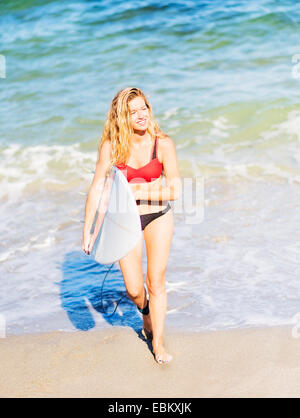 Ee.Uu., Florida, Júpiter, Retrato de mujer joven caminando en surf, llevando las tablas de surf Foto de stock