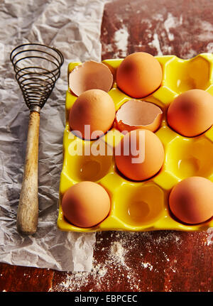 Vintage batir claras de huevo amarilla junto al titular sobre papel pergamino sobre una tabla de madera cubierto de harina Foto de stock