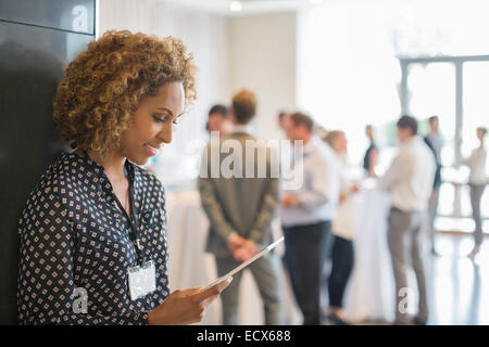 Mujer joven con apoyándose en la pared mientras mantiene tableta digital