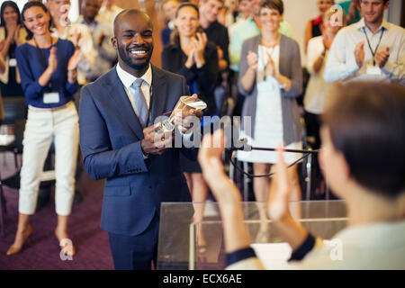 Retrato de joven sosteniendo el trofeo, de pie en la sala, sonriendo a aplaudir a audiencia Foto de stock