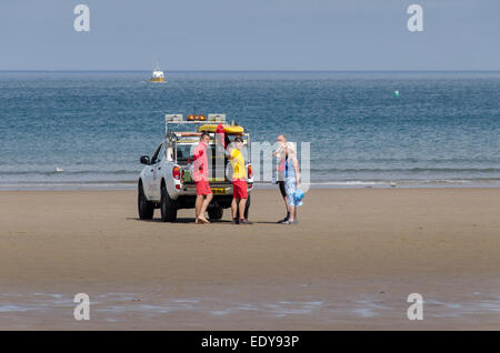 2 macho salvavidas RNLI por 4x4 permanente vehículo patrullero hablar y dar consejos a una pareja de turistas - Whitby Beach, North Yorkshire, Inglaterra.