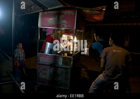 Dos hombres en una motocicleta están comprando pollo frito de un vendedor callejero en una calle de la ciudad de Kampong Cham, Camboya.