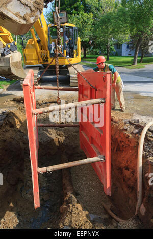 Trabajador de la construcción colocando las entibaciones en el agujero con la excavadora Foto de stock