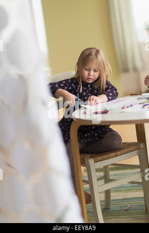 Chica (4-5) jugando en una mesa en una habitación familiar Foto de stock