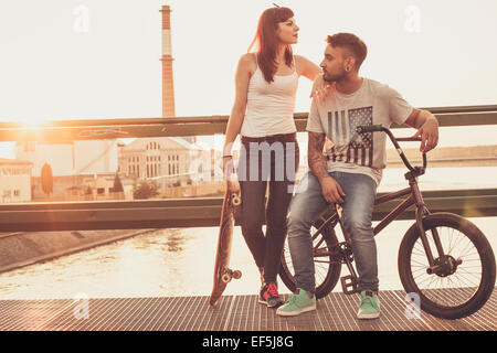 Pareja joven con skate y bicicletas BMX descansando en el puente