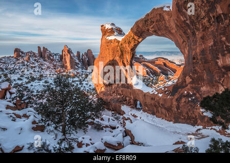 Arco doble de O a 65 pies de altura autoestable arco natural cubierto de nieve durante el invierno atardecer en el Parque Nacional de Los Arcos, cerca de Moab, Utah.