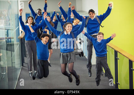 Estudiantes de secundaria entusiasta vistiendo uniformes escolares sonriendo y saltando en el corredor de la escuela Foto de stock