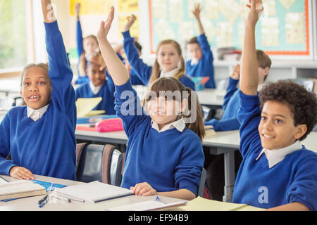 Los niños de escuela primaria vistiendo uniformes escolares azul levantando las manos en el aula Foto de stock