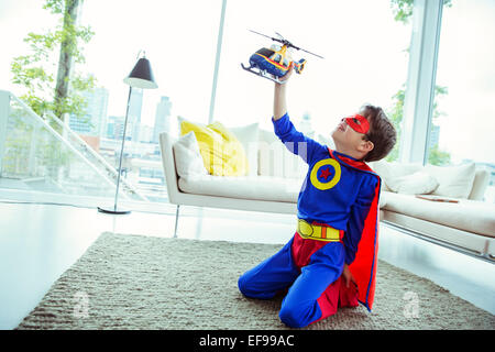 Superhéroe boy jugando con helicóptero de juguete en la sala de estar
