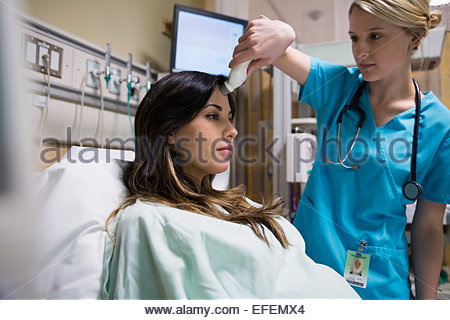 Enfermera con termómetro frontal en la mujer embarazada