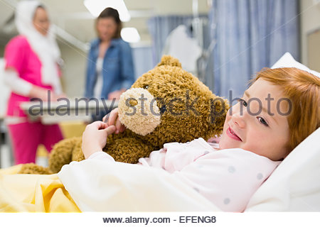 Chica abrazando a oso de peluche en la cama de un hospital