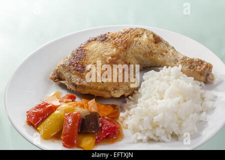 Muslo de pollo asado con arroz y verduras en una placa blanca.