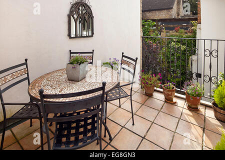Balcón pequeño con suelos de baldosas de terracota, ollas y asientos de metal al aire libre, jardín, Oxfordshire, Inglaterra Foto de stock