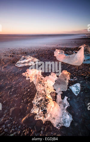 Roto el hielo de los icebergs se lavan en la playa al amanecer negro Jokulsarlon Jokulsarlon sudeste de Islandia Foto de stock