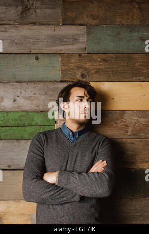 Apuesto joven hombre de negocios apoyado contra una pared de madera con sus brazos cruzados mirando a otro lado.