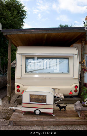 Trailer campamento bajo un cobertizo con remolque y un perro pequeño visible en primer plano. Foto de stock