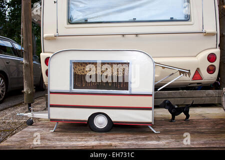 Modelo diminuto caravana por un pequeño perro mascota estacionado en la parte posterior de los propietarios a tamaño completo en una caravana en un camping. Foto de stock
