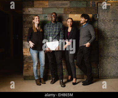 Retrato de los profesionales jóvenes riendo mientras está de pie juntos en la oficina. Multiétnico equipo empresarial busca felices juntos.
