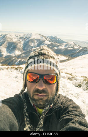 Hombre con gafas de sol posa con esquí y otros equipos en la cima de la  montaña