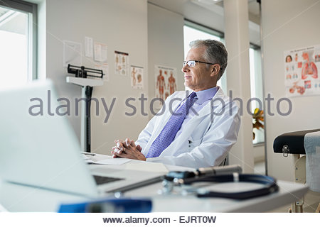 Pensativo médico sentados frente al escritorio en la oficina de la clínica